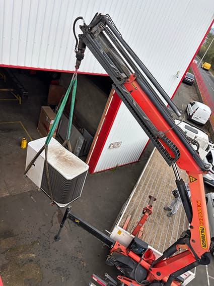 Camion-grue levant une unité de pompe à chaleur air/eau sur le site Legrand de Quincieux
