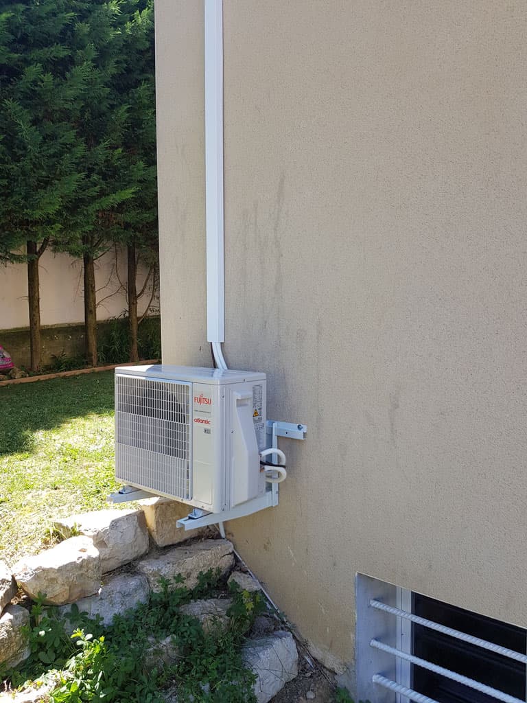 Unité extérieure d'une pompe à chaleur air/air réversible fixée en façade sur console murale, à Parcieux